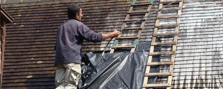 Artisan traitant à l'hydrofuge une toiture 